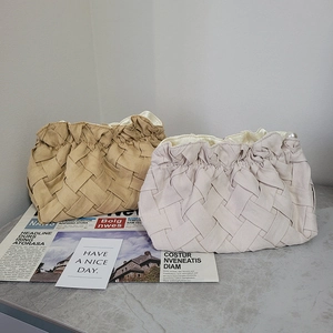Detail of woven khaki and beige clutch bags with pleats and pearl accent on marble