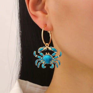 Detail of a blue enamel crab charm earring with a gold hoop on a female model