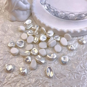 Close-up of irregular baroque pearl nail art charms on white textured background