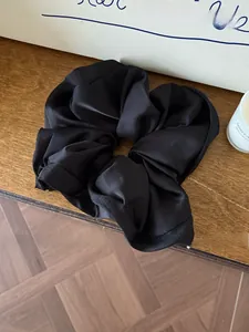 Detail shot of a black satin scrunchie with soft folds on a wooden desk setting