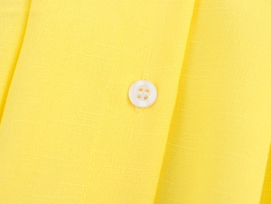 Detail of yellow fabric texture and a white four-hole button on the long-sleeve blouse