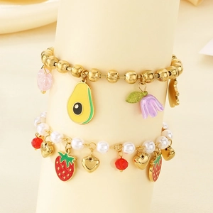 Detail of fruit charms on gold bead and pearl bracelets featuring avocado and strawberry