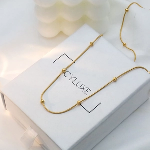 Detail of 18k gold plated snake chain necklace with beads on a white jewelry box