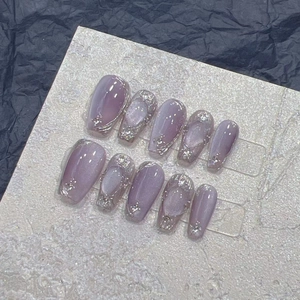 Detail of purple cat-eye press-on nails with silver foil on a textured stone surface