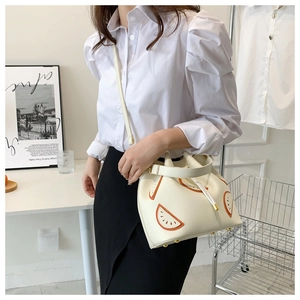 Lifestyle shot of white drawstring bucket bag with orange fruit patch and metal hardware