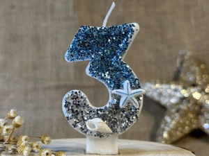 Macro shot of blue and silver glitter number 3 candle with starfish and shell details
