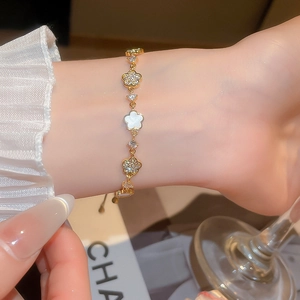 Detail of elegant gold flower charm bracelet with white shell clover on female wrist
