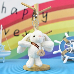 Close-up detail of a soft white plush bunny keychain featuring a tiny brown crossbody bag.