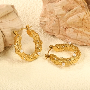 Golden textured hoop earrings with small pearls and crystals on a stone background