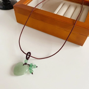 Macro detail of heart-shaped jade pendant with small beads on a woven red cord