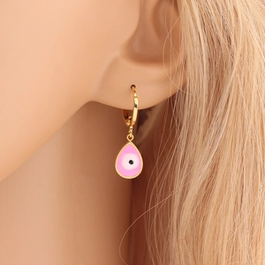 Close-up of gold hoop earring with pink teardrop evil eye pendant worn by a model