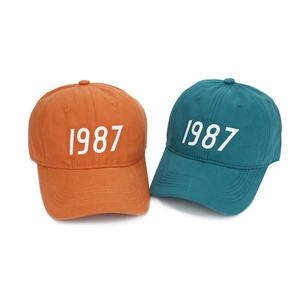 Detailed view of 1987 embroidery on high-quality orange and teal cotton baseball caps