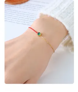 Detail of red rope and gold chain bracelet with a green gemstone on a model's wrist