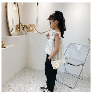 Dettaglio outfit estivo bimba con top a volant, pantaloni e borsa in paglia margherita