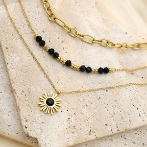 Three-layer gold necklace with black beads and a sun pendant on textured stone