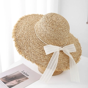 Dettaglio cappello di paglia con fiocco di garza bianca, perle e tesa a frange per mare
