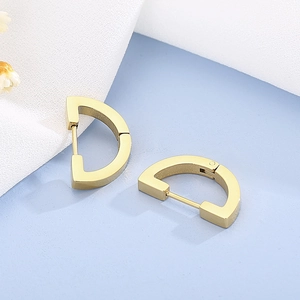 Detail of gold D-shape geometric earrings with smooth metallic finish on light blue background