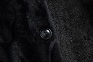 Macro detail of high-quality black faux fur fabric with a round sewn button on the overcoat