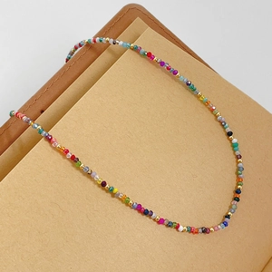 Primo piano di una collana girocollo di perline colorate con dettagli dorati su un taccuino