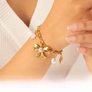 Detail of gold chain bracelet with pearl bow, star pendant, and droplet pearl on a wrist
