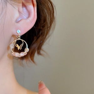 Close-up of golden butterfly hoop earring with pink crystals on model ear