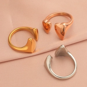 Three heart-shaped open rings in gold, rose gold and silver on pink silk fabric background
