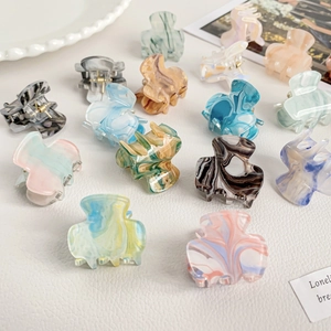Colorful acrylic mini hair claws with marble texture patterns on white leather background