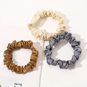Detailed view of three satin scrunchies in beige, bronze, and dark grey on aesthetic paper