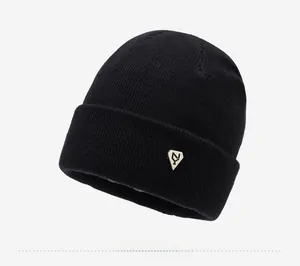 Detailed close-up of a black knit beanie with a diamond-shaped metal logo plaque