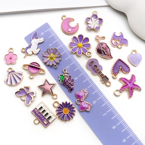 Purple enamel pendants in various shapes with a ruler for size reference and scale