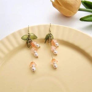 Pink bellflower dangle earrings with green leaves and pearls on a ceramic plate