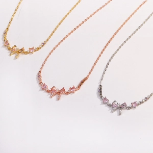 Detailed view of bow and heart necklaces in gold, rose gold, and silver finishes