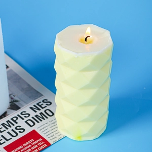 Macro detail of a yellow cylindrical candle with a textured diamond pattern and lit wick