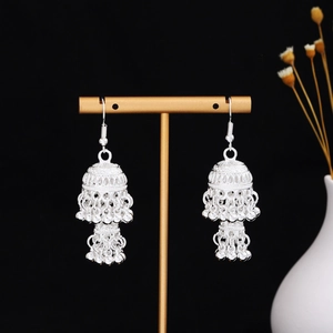 Dettaglio di orecchini etnici in argento con motivi traforati e nappe con piccole sfere
