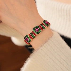 Close-up of vintage gold bracelet with green enamel and red gems on a model's wrist