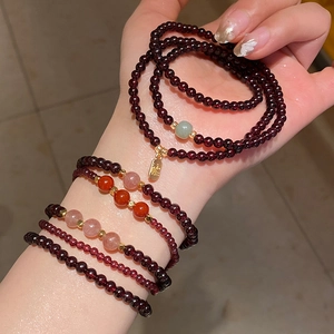 Detail of layered garnet and strawberry quartz bracelets with a golden Fu pendant
