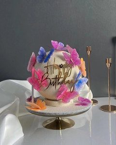 Detailed view of spherical birthday cake with watercolor butterflies and gold topper