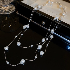 Detailed macro view of layered baroque pearls and silver chains on a black reflective surface