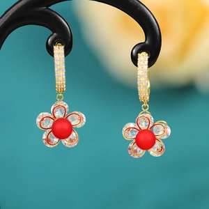 Detail of flower earrings with gold petals and a red pearl center on a black display stand