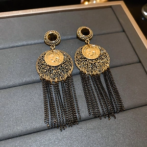 Vue détaillée de boucles d'oreilles vintage en bronze avec pièce et pompons noirs