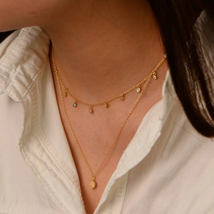 Close-up of gold double-layer necklace featuring zircon dots and oval pendant detail