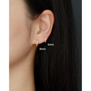 Detailed close-up of 6mm and 8mm gold wave pavé crystal huggie earrings on model