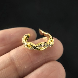 Macro view of gold twisted ear cuff with inlaid zircons held between fingers