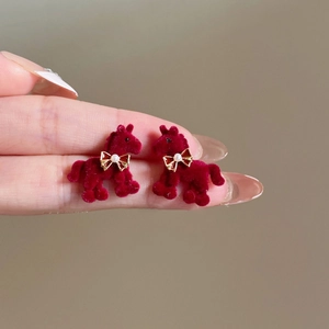 Detailed close-up of red flocked pony stud earrings with gold pearl bow accents