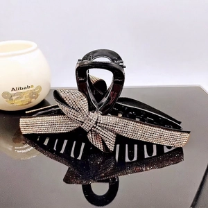 Elegant black bow hair claw clip with champagne rhinestones on a reflective surface