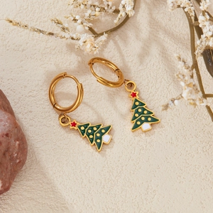 Festive gold earrings with green enamel Christmas trees on a textured ivory background