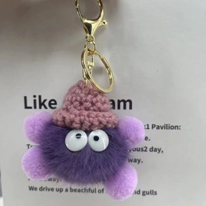 Close-up of purple plush keychain with a pink knit hat and golden lobster clasp detail