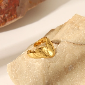 Macro shot of gold irregular wave pattern ring on natural stone showing hammered texture