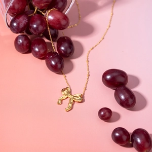 Close-up of 18k gold plated stainless steel bow necklace among red grapes and glass
