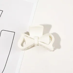 Detail shot of a matte white bow hair claw clip showing fine teeth and spring structure